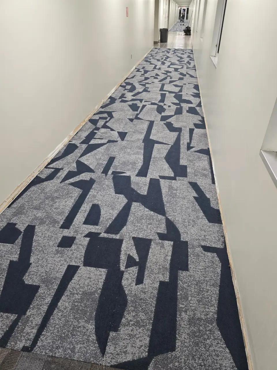 Navy and gray abstract-pattern carpet tile installed in a long commercial corridor
