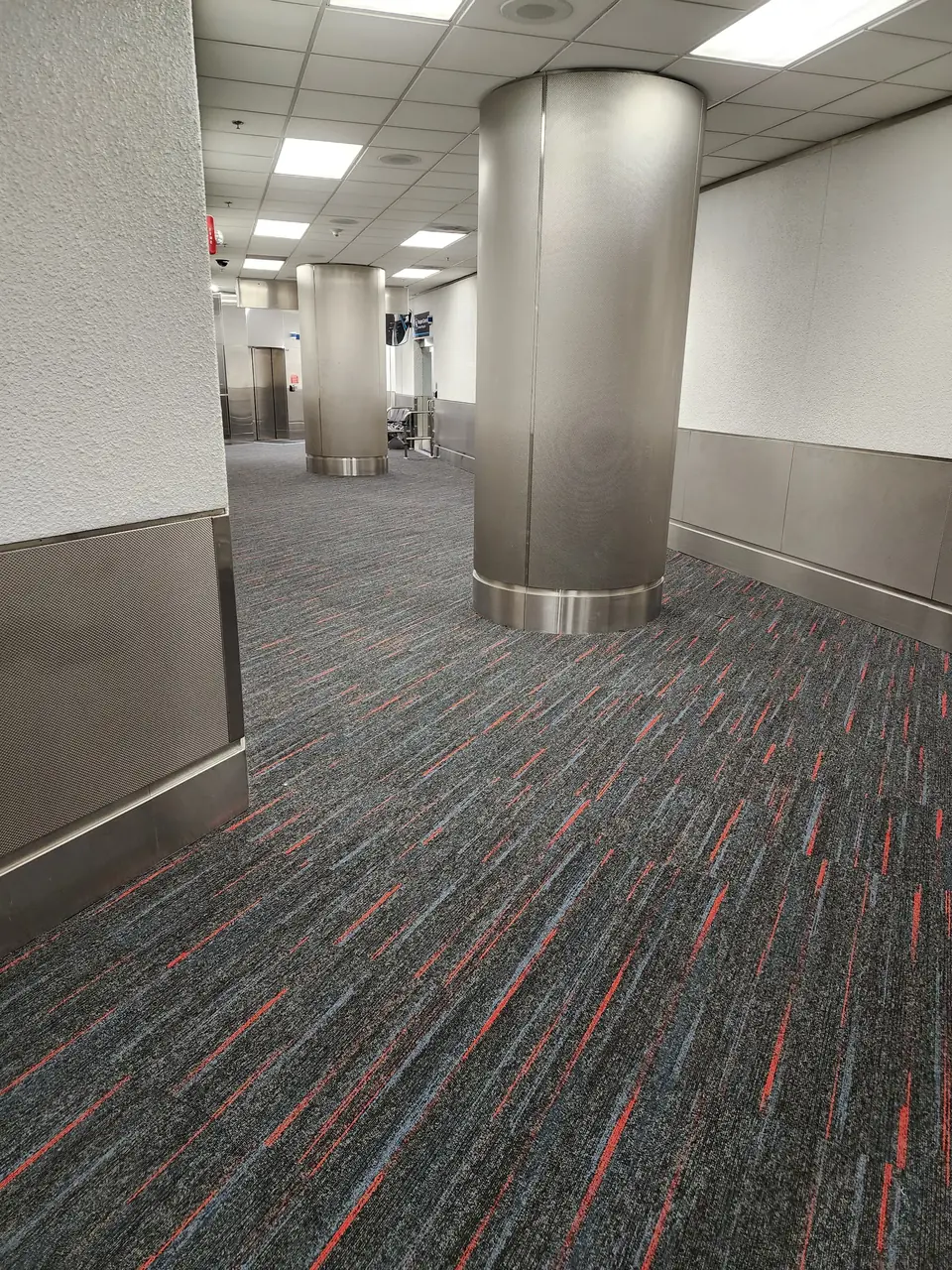 Charcoal carpet tile with red and blue accents around stainless steel columns at MIA