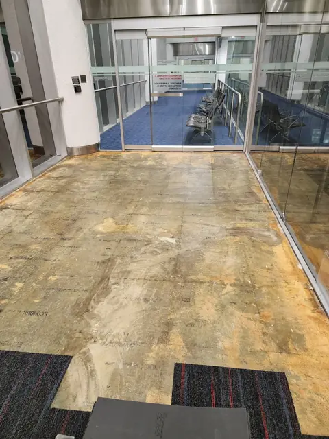 Prepared substrate in a glass-walled airport corridor before new carpet tile