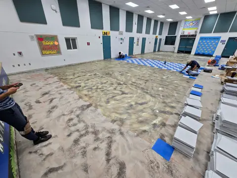 Installers setting VCT over fresh adhesive in a school cafeteria